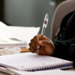 A hand holding a pen poised over a notebook