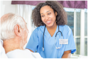 Standing African American female nurse with stethoscope smiling at older white male patient in bed