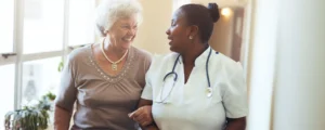 Older white woman linking arms with African American female nurse