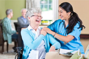 Female nurse laughing with older woman patient seated in wheelchair
